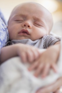 Close up of baby boy (2-5 months) sleeping in mother's arms.
