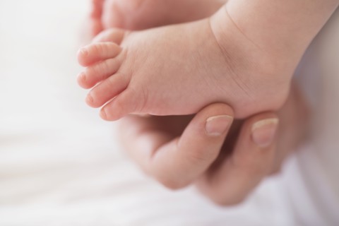 Close up of mother's hand touching baby boy's(2-5 months) foot.