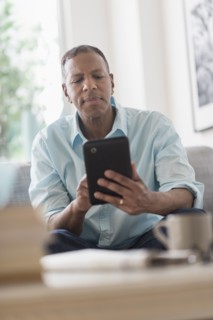 Man sitting on sofa at home and using digital tablet.