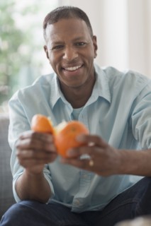 Portrait of smiling man peeling orange fruit.