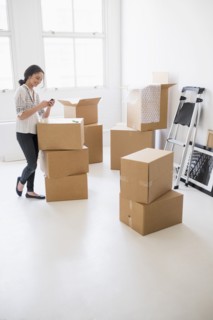 Young woman standing among boxes in new home and using mobile phone.