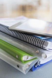 Close up of stack of notebooks with digital tablet on top.