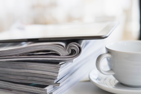 Close up of coffee cup and digital tablet on top of magazine stack.