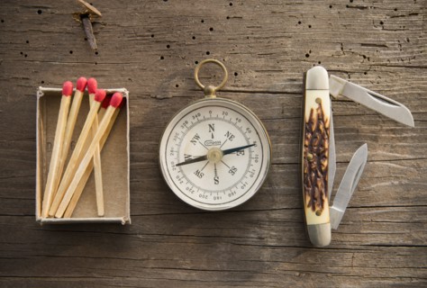 Studio Shot of matchsticks, compass and knife on wooden board.
Photo : Jamie Grill