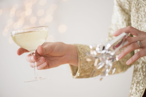 Studio Shot of female's hands holding champagne and noisemaker.
Photo : Jamie Grill