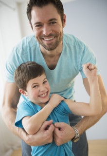 Father embracing son (8-9), Boy flexing muscles.
Photo : Jamie Grill