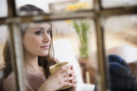 Young woman contemplating in living room with coffee cup in hands.
Photo : Jamie Grill