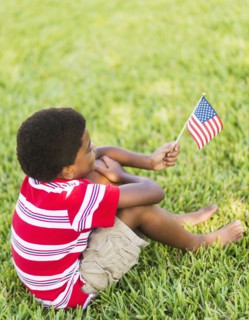 boy (6-7) sitting on grass and holding american flag.
Photo : Daniel Grill