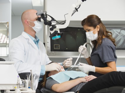 Dentist operation on patient and using microscope.