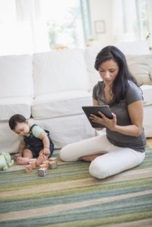 Mother using tablet pc while her son (6-11 months) playing with building blocks.