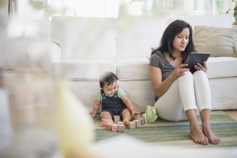 Mother using tablet pc while her son (6-11 months) playing with building blocks.