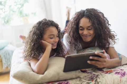 Mother with daughter (8-9) using digital tablet on bed.