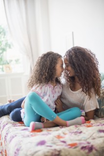 Mother and daughter (8-9) rubbing noses on bed.
