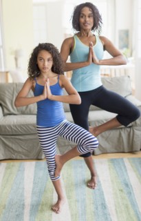 Mother and daughter (8-9) doing in yoga poses in living room.