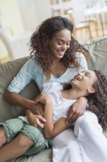 Mother tickling daughter (8-9) on sofa.