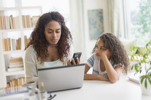 Mother and daughter (8-9) using laptop and smart phone.