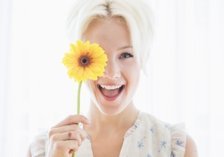 Portrait of blonde woman holding yellow flower.