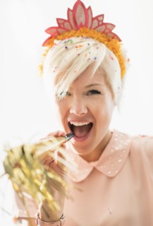 Woman wearing tiara blowing party horn blower.