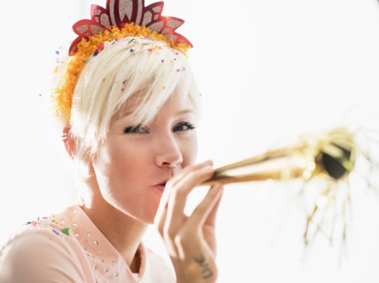 Woman wearing tiara blowing party horn blower.