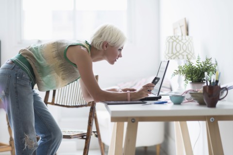 Woman using laptop and cell phone at home.