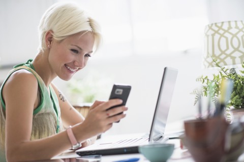 Woman using cell phone and laptop at home.