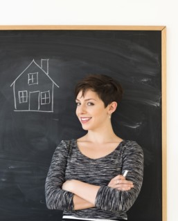Woman in front of blackboard with house drawing.