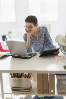 Senior business woman using cell phone and tablet pc in office.