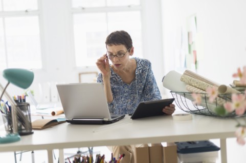 Senior business woman using laptop and tablet in office.