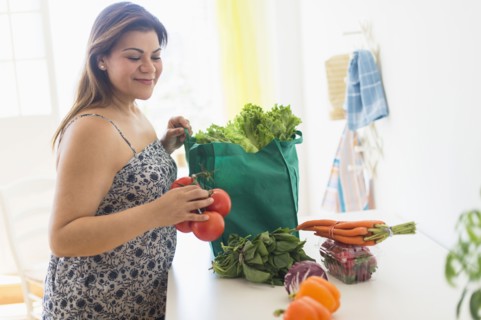Woman taking out vegetables of grocery bag.