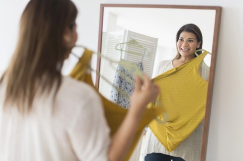 Woman holding new dress and looking at mirror.