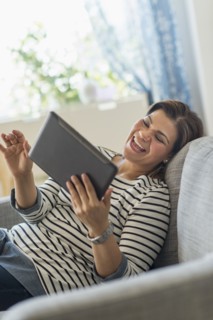 Portrait of happy woman lying on sofa with tablet pc.