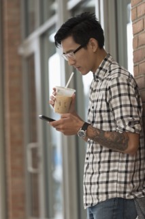 Man walking on sidewalk with iced coffee and mobile phone.