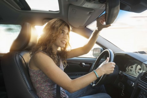 Young woman adjusting rear view mirror while driving.