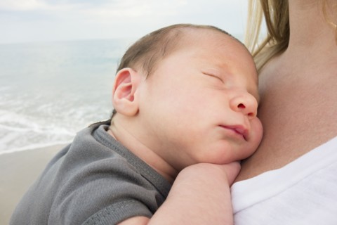 Mother holding newborn daughter on beach