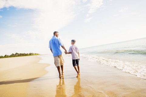 Father and son (10-11) walking on beach