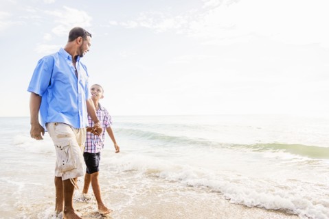 Father and son (10-11) walking on beach