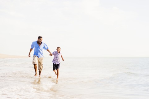 Father and son (10-11) running on beach