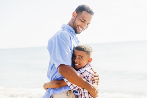 Father and son (10-11) embracing on beach