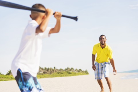 Father and son (10-11) playing baseball on beach