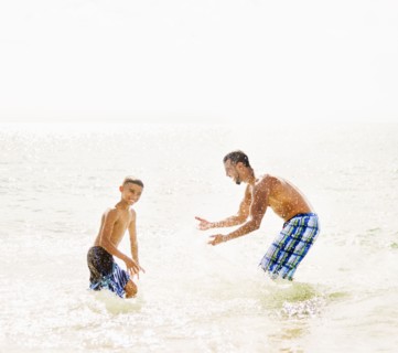 Father and son (10-11) having fun on beach