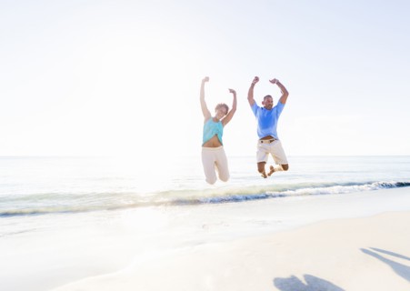 Mature couple jumping in sea with arms raised