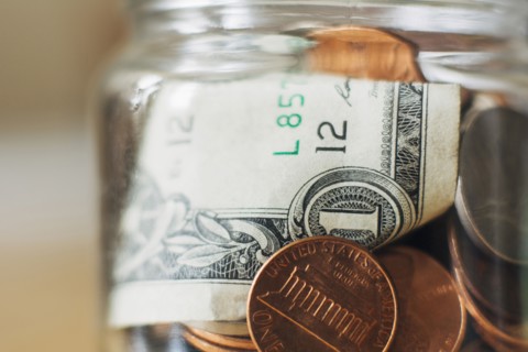Studio shot of jar filled with coins and one dollar banknote, close up