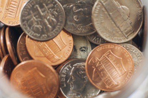 Studio shot of jar filled with coins and one dollar banknote, close up