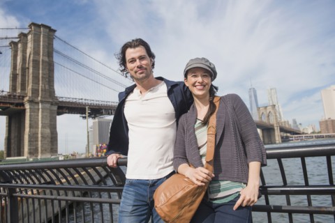 Couple leaning against railing and looking at camera. Brooklyn, New York.