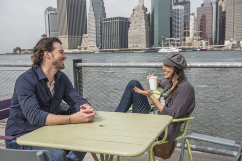 Happy couple sitting and discussing with cityscape in background. Brooklyn, New York.
