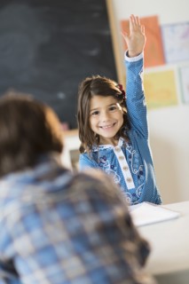 Pupils (6-7) learning in classroom, Girl (6-7) raising hand.