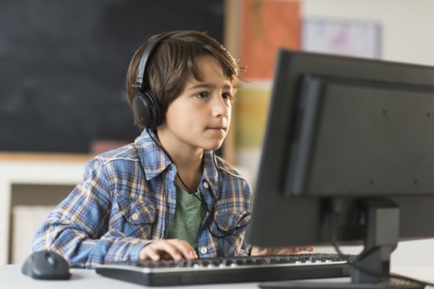Schoolboy (6-7) using computer in classroom.