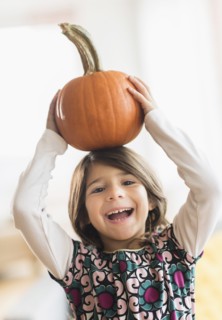 Portrait of happy girl (6-7) with pumpkin on head.