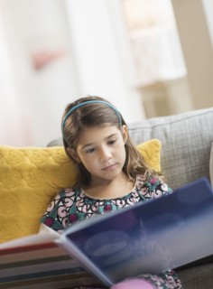 Girl (6-7) reading book at home.