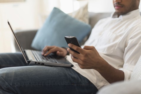 Man sitting in living room, using laptop and cell phone.